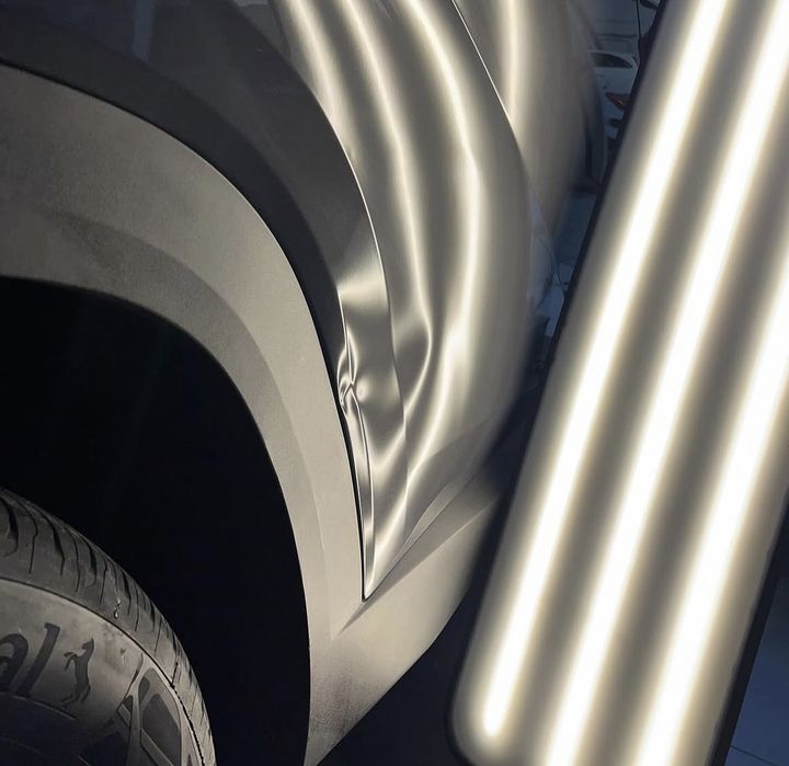 Aile avant grise pliée à l'arête du passage de roue, sous la lampe