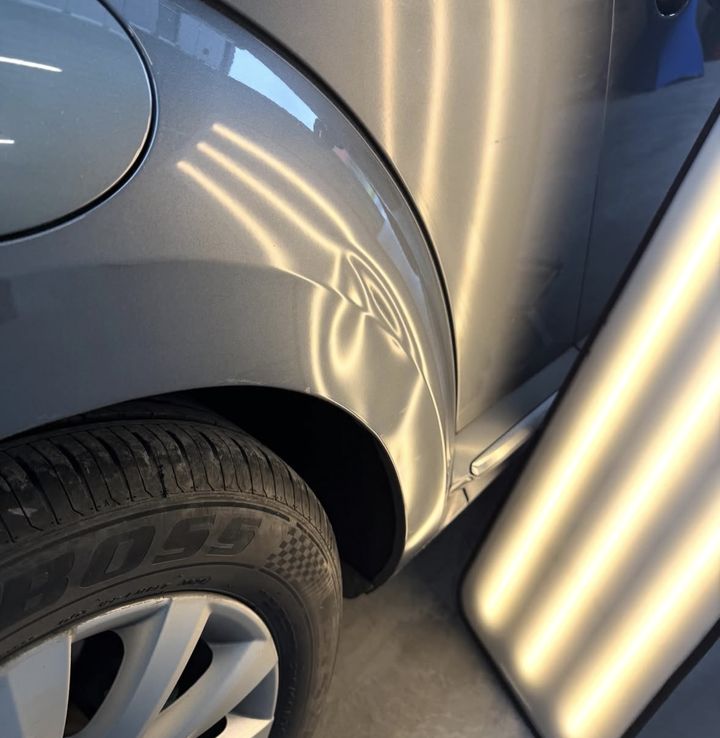 Aile arrière grise de VW bossée au bord du passage de roue, sous la lampe